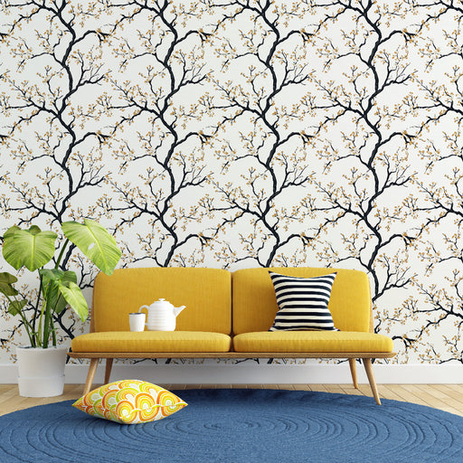 Un salon lumineux avec un papier peint représentant des branches noires ornées de fleurs dorées sur fond blanc, créant une atmosphère douce et accueillante.