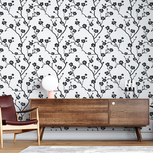 Un salon contemporain avec un papier peint floral noir et blanc représentant des branches délicates, créant une ambiance élégante et apaisante.