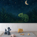 Une chambre d'enfant avec un papier peint nocturne représentant un caméléon vert sous un ciel étoilé, créant une atmosphère ludique et apaisante.