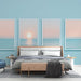 Une chambre apaisante avec un papier peint bleu clair, agrémentée de trois tableaux représentant un coucher de soleil sur la mer, créant une ambiance sereine et relaxante.