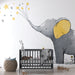 Une chambre d'enfant avec un papier peint illustrant un éléphant gris aux grandes oreilles jaunes, entouré d'étoiles dorées, créant une ambiance douce et ludique.