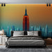 Une chambre moderne avec un papier peint représentant une silhouette urbaine colorée, mettant en avant l'Empire State Building sur un dégradé chaleureux.