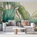 Un salon moderne avec un papier peint représentant de grandes feuilles tropicales aux teintes vertes et turquoise sur un fond clair, créant une ambiance fraîche et apaisante.
