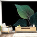 Un salon moderne avec un papier peint représentant de grandes feuilles stylisées vertes et blanches sur un fond noir, créant une ambiance élégante et apaisante.