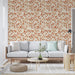 Un salon lumineux avec un papier peint aux motifs de feuilles dans des teintes chaudes de rouge et beige, créant une atmosphère chaleureuse et accueillante.