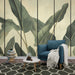 Un salon moderne avec un papier peint tropical représentant de grandes feuilles vertes sur un fond clair, créant une atmosphère apaisante et naturelle.