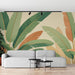 Un salon moderne avec un papier peint tropical aux grandes feuilles vertes et ocres sur fond beige, créant une ambiance chaleureuse et naturelle.