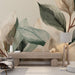 Une pièce moderne avec un papier peint aux motifs de grandes feuilles stylisées dans des teintes douces de vert, beige et marron créant une atmosphère apaisante et naturelle.