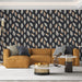 Un salon contemporain avec un papier peint aux motifs de feuilles stylisées sur fond noir, mêlant des teintes dorées et blanches, créant une ambiance chaleureuse et élégante.