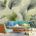 Un salon moderne avec un papier peint représentant de grandes feuilles stylisées en vert et noir sur fond beige, créant une atmosphère apaisante et naturelle.