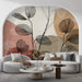 Un salon moderne avec un papier peint aux motifs de feuilles stylisées en noir sur un fond aux teintes douces de beige et terracotta, créant une ambiance chaleureuse et artistique.
