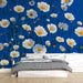 Une chambre lumineuse avec un papier peint floral sur fond bleu, ornée de grandes marguerites blanches et jaunes, créant une atmosphère joyeuse et apaisante.