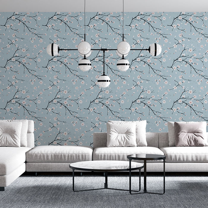 Un salon moderne avec un papier peint bleu clair orné de branches noires et de délicates fleurs roses, créant une atmosphère douce et apaisante.
