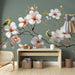 Une pièce lumineuse avec un papier peint floral représentant de grandes fleurs blanches et des oiseaux colorés sur un fond vert apaisant.