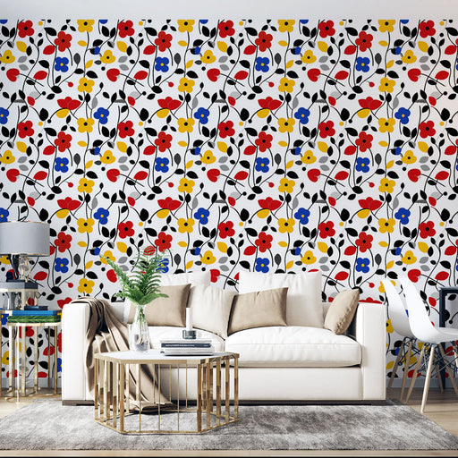 Un salon lumineux avec un papier peint floral coloré aux motifs de fleurs rouges, jaunes, bleues et noires sur fond blanc, créant une ambiance joyeuse et dynamique.