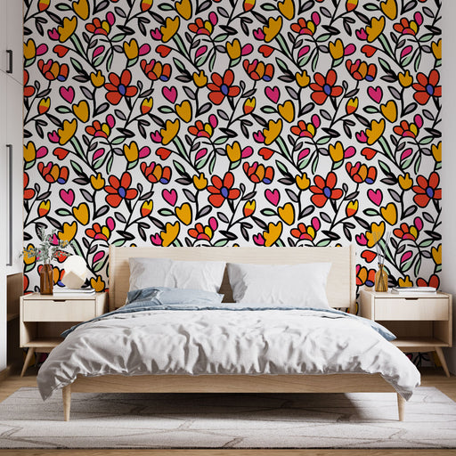 Une chambre lumineuse avec un papier peint floral coloré aux motifs de fleurs rouges, jaunes et roses sur fond blanc, créant une atmosphère joyeuse et dynamique.