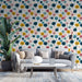 Un salon moderne avec un papier peint coloré représentant des arbres stylisés aux teintes vives de rose, jaune et bleu sur fond clair, créant une atmosphère joyeuse et dynamique.