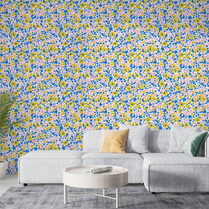 Un salon lumineux avec un papier peint floral coloré aux motifs de fleurs jaunes, roses et bleues sur fond blanc, créant une ambiance joyeuse et accueillante.