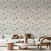 Un salon lumineux avec un papier peint floral aux teintes douces de rose et vert sur fond clair, créant une atmosphère apaisante et accueillante.