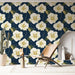 Un salon lumineux avec un papier peint floral aux grandes fleurs blanches et feuilles vertes sur fond bleu marine, créant une ambiance tropicale et accueillante.