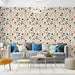 Un salon lumineux avec un papier peint à motifs floraux délicats sur fond beige, mêlant des teintes de vert, noir et terracotta pour une ambiance chaleureuse et moderne.