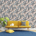 Un salon lumineux avec un papier peint floral aux motifs de fleurs roses et noires sur fond blanc, créant une ambiance joyeuse et accueillante.