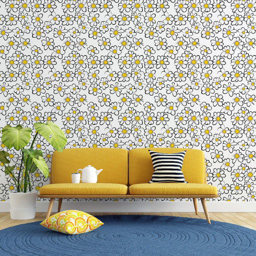 Un salon lumineux avec un papier peint floral aux motifs de marguerites blanches et jaunes sur fond clair, créant une ambiance joyeuse et accueillante.