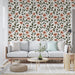 Un salon lumineux avec un papier peint floral aux motifs de fleurs roses et de feuilles vert foncé sur fond clair, créant une atmosphère chaleureuse et accueillante.