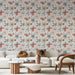 Un salon lumineux avec un papier peint floral aux teintes douces de rose, bleu et jaune, créant une atmosphère chaleureuse et accueillante.