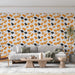 Un salon moderne avec un papier peint aux motifs de feuilles ginkgo en orange et noir sur fond blanc, créant une ambiance chaleureuse et dynamique.