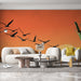 Un salon moderne avec un papier peint dégradé orange représentant des oiseaux en vol, créant une atmosphère dynamique et chaleureuse.