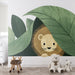 Une chambre d'enfant avec un papier peint illustrant un lion mignon caché derrière de grandes feuilles vertes, créant une ambiance ludique et chaleureuse.