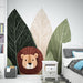 Une chambre d'enfant avec un papier peint illustrant un lion mignon entouré de grandes feuilles stylisées dans des teintes vertes et beige, créant une ambiance ludique et chaleureuse.