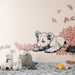Une chambre d'enfant avec un papier peint illustrant un lionceau noir et blanc entouré de feuilles roses, créant une ambiance douce et ludique.