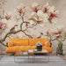 Une salon lumineux avec un papier peint floral représentant de grandes fleurs de magnolia et des oiseaux sur un fond beige, créant une atmosphère douce et apaisante.