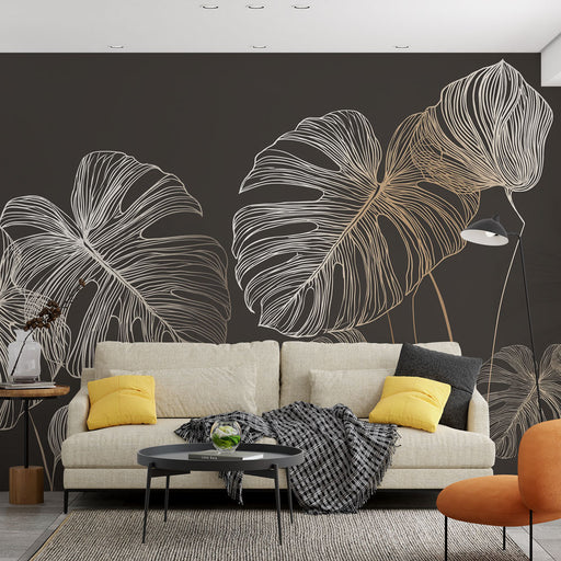 Un salon moderne avec un papier peint représentant de grandes feuilles de monstera en lignes blanches et dorées sur fond noir, créant une ambiance élégante et chaleureuse.