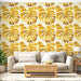 Un salon moderne avec un papier peint tropical aux grandes feuilles monstera dorées sur fond clair, créant une ambiance chaleureuse et ensoleillée.