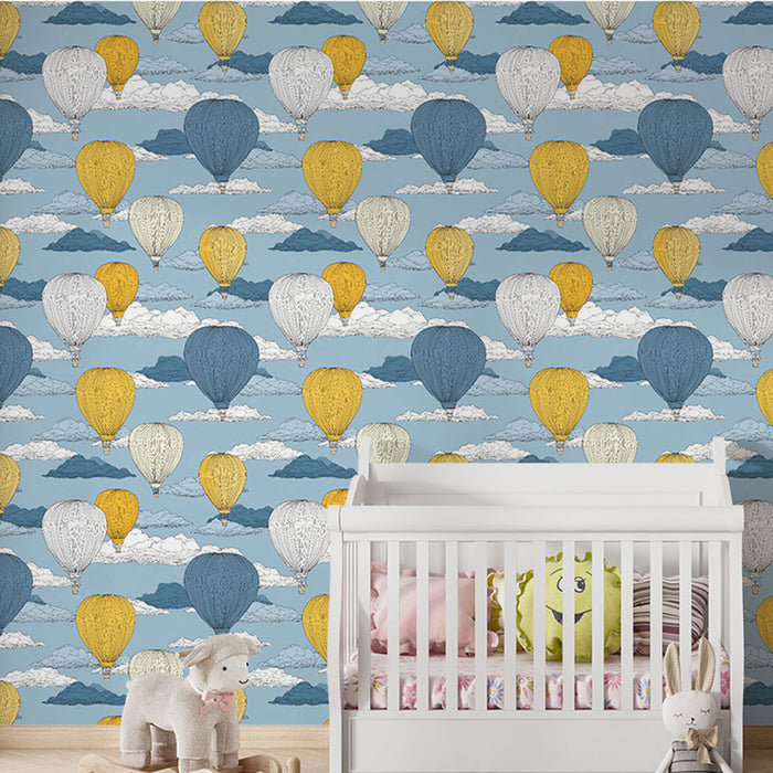 Une chambre d'enfant avec un papier peint illustrant des montgolfières colorées sur fond bleu, créant une atmosphère joyeuse et rêveuse.