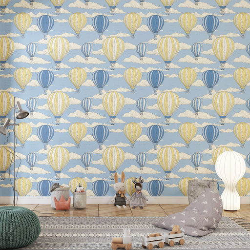 Une chambre d'enfant avec un papier peint illustrant des montgolfières jaunes et bleues flottant parmi des nuages sur un fond bleu clair, créant une ambiance joyeuse et aérienne.