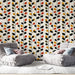 Un salon moderne avec un papier peint aux motifs de feuilles stylisées en noir, rouge, jaune et vert sur fond clair, créant une ambiance chaleureuse et dynamique.
