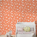 Une chambre d'enfant avec un papier peint coloré orange orné de nuages blancs et d'étoiles dorées, créant une atmosphère joyeuse et rêveuse.