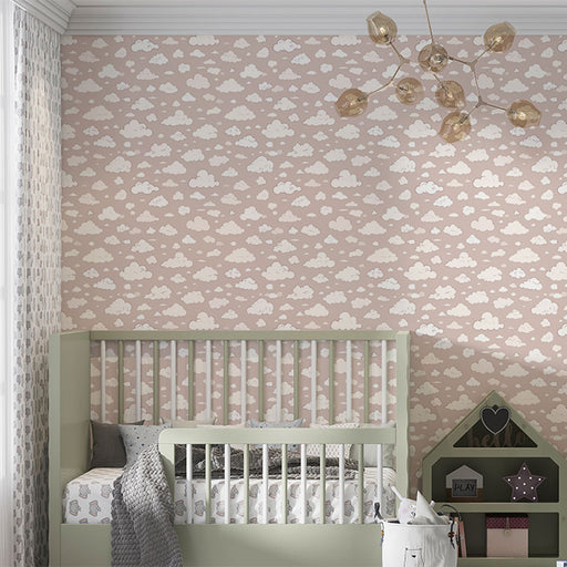 Une chambre d'enfant avec un papier peint rose pâle orné de nuages blancs, créant une atmosphère douce et rêveuse.