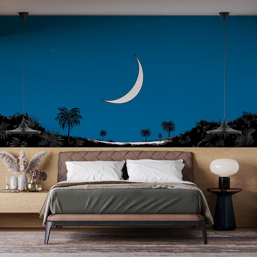 Une chambre moderne avec un papier peint représentant un paysage nocturne bleu, une lune blanche et des palmiers noirs créant une atmosphère sereine et rêveuse.