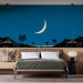Une chambre moderne avec un papier peint représentant un paysage nocturne bleu, une lune blanche et des palmiers noirs créant une atmosphère sereine et rêveuse.