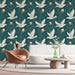 Un salon moderne avec un papier peint illustrant des oiseaux blancs en vol sur fond vert profond, agrémenté de branches et d'œufs dorés, créant une ambiance chaleureuse et accueillante.