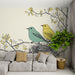 Un salon lumineux avec un papier peint illustrant des oiseaux turquoise et jaune perchés sur des branches, créant une atmosphère joyeuse et naturelle.