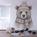 Une chambre d'enfant avec un papier peint illustrant un ours au bonnet et à l'écharpe pastel, créant une ambiance douce et chaleureuse.