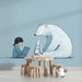 Une chambre d'enfant avec un papier peint illustratif représentant une petite fille lisant à côté d'un ours polaire sur fond bleu apaisant.