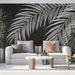 Un salon moderne avec un papier peint noir orné de grandes feuilles blanches de palmier, créant une atmosphère élégante et tropicale.