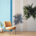 Un salon lumineux avec un papier peint à rayures blanches et une ombre de palmier, évoquant une ambiance tropicale et relaxante.